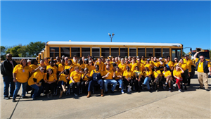 large group of adults in gold shirts in front of school bus